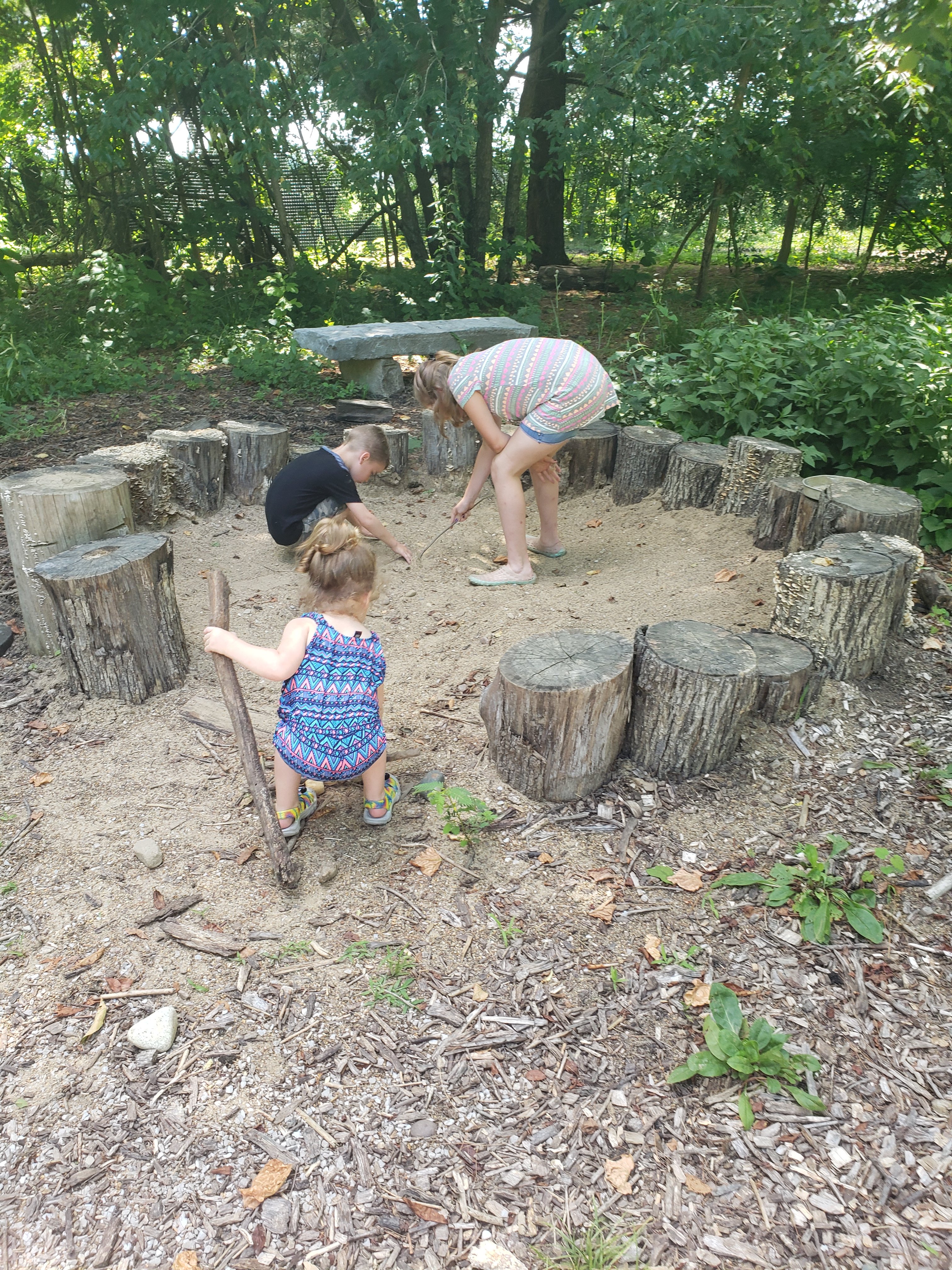 Three kids playing in a sandpit made with a stump border in Wesselman Woods Nature Playscape in Evansville, Indiana  Things to do with kids in Evansville Indiana. Kids activities in Evansville 