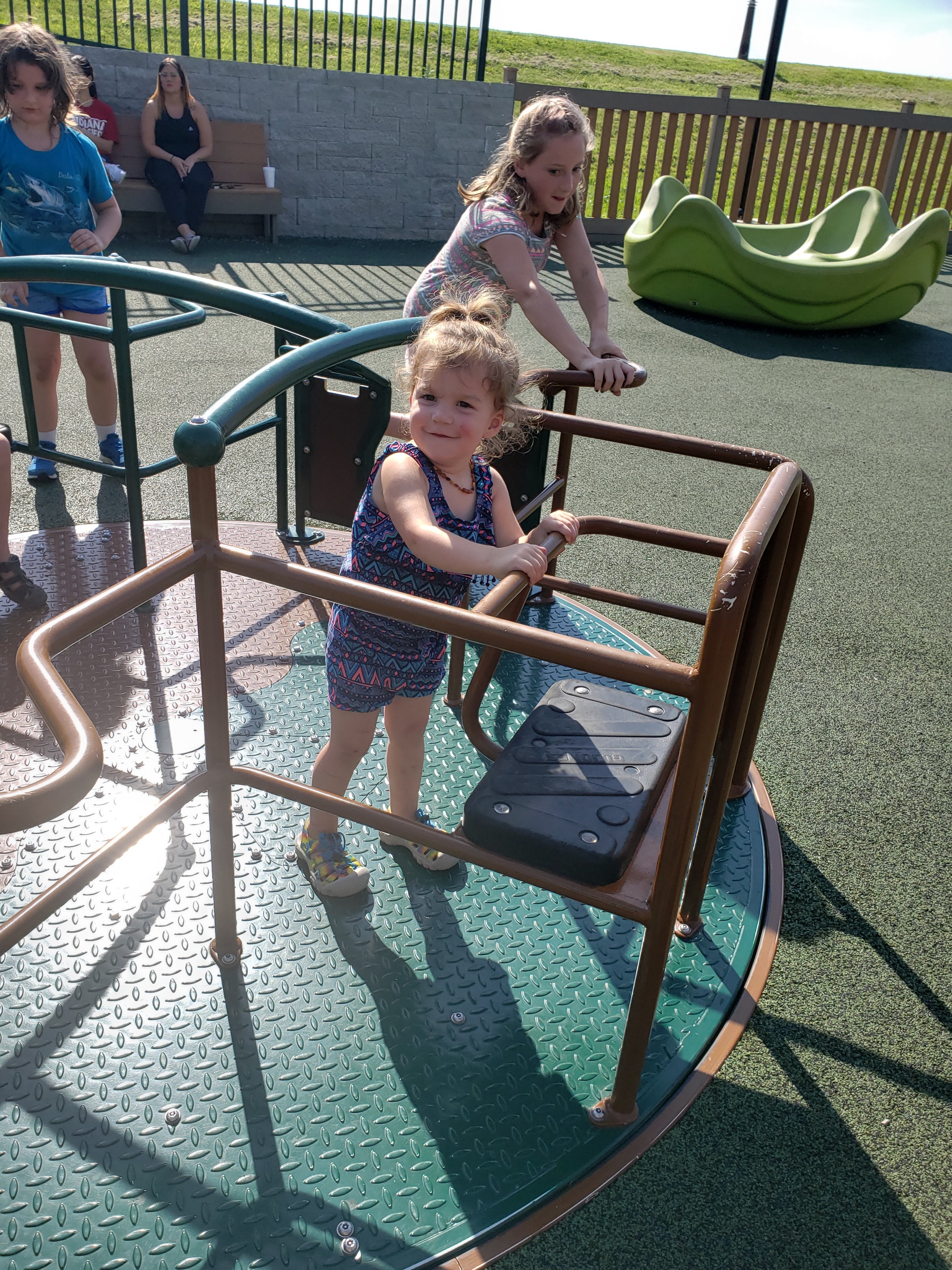 Photo of toddler girl smiling with older girl in background playing on equipment at Mickey's Kingdom Park for Kids in Evansville, Indiana  Things to do with kids in Evansville Indiana. Kids activities in Evansville  