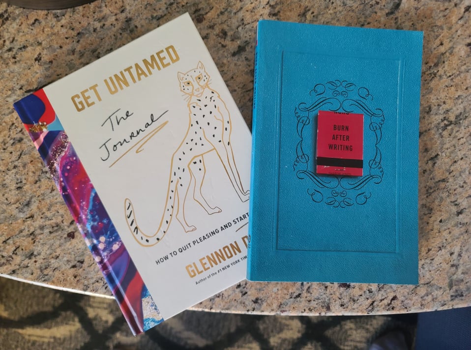 The "Get Untamed The journal" and "Burn After Writing" journals laying closed on a table top