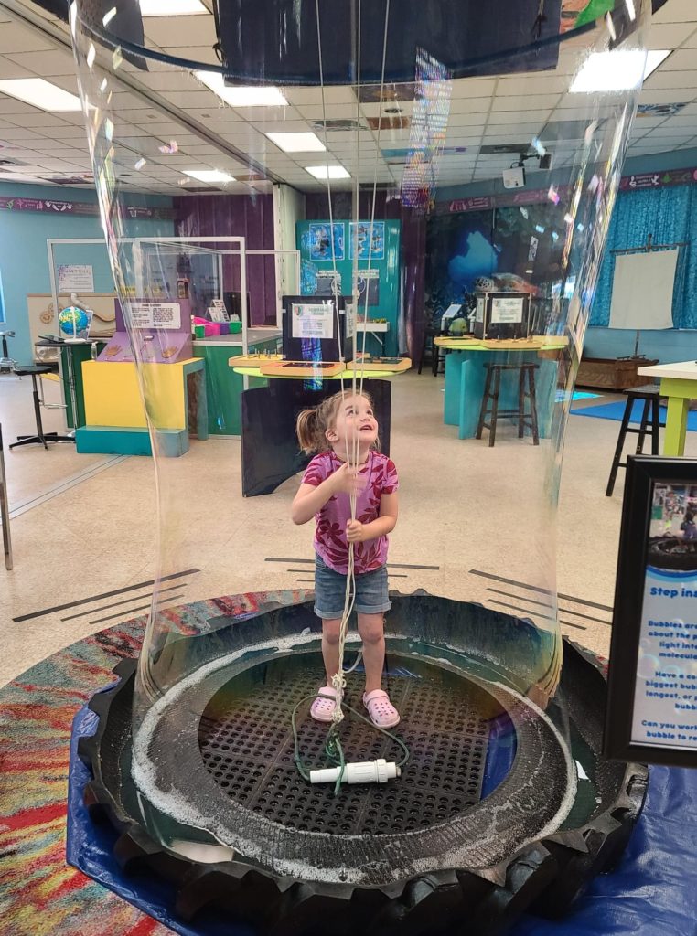 young girl standing in the middle of a large bubble at a science center free summertime activities for kids 