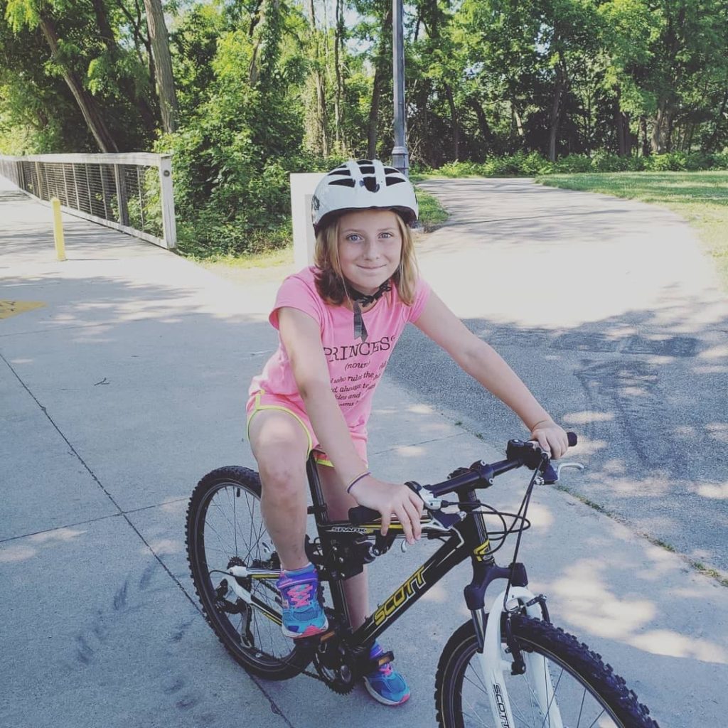 a girl wearing a white bike helmet on a black bike on a sidewalk