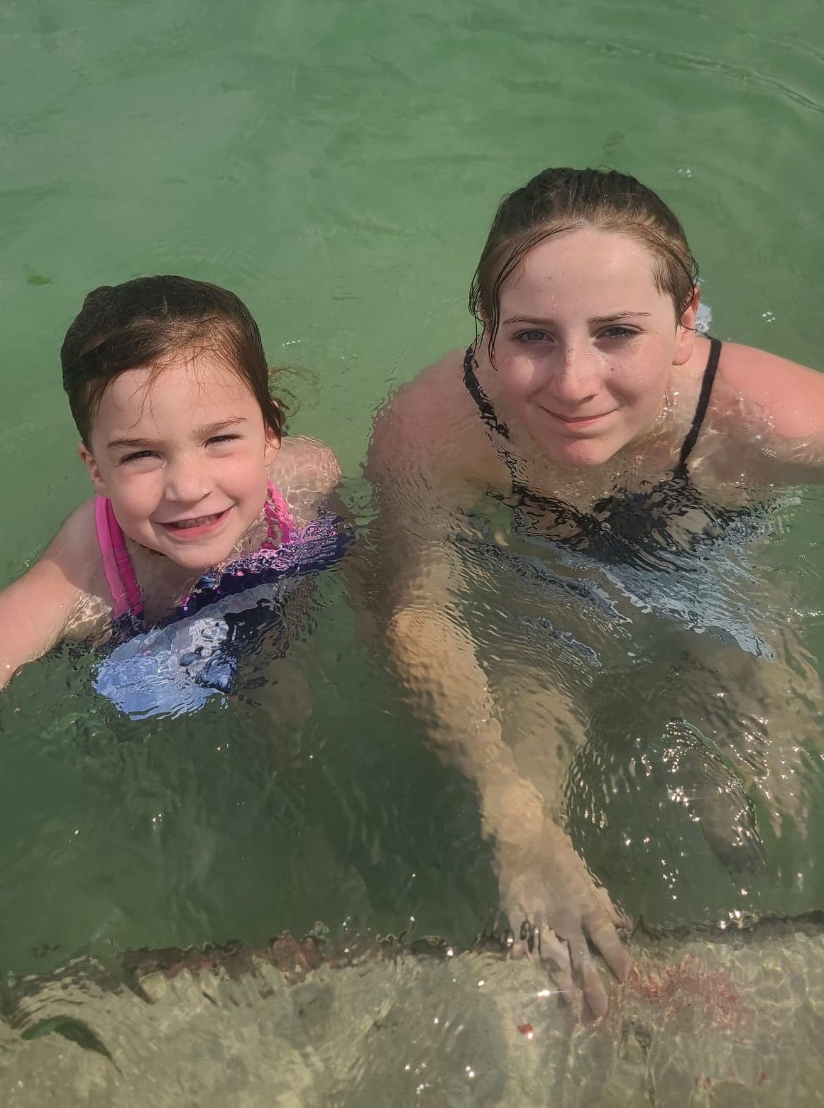 two girls in water up to their shoulders smiling