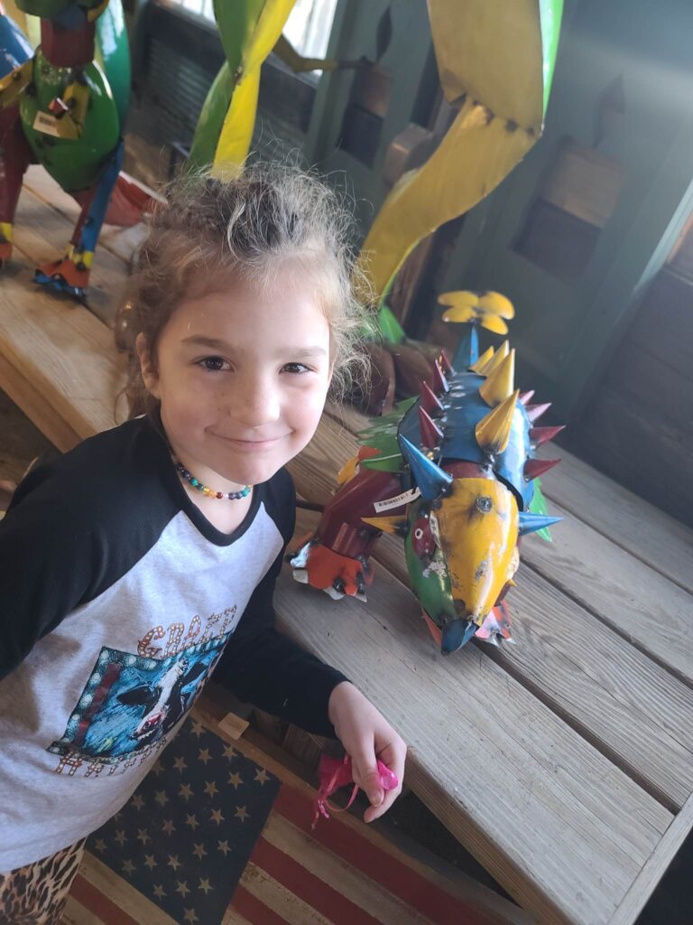 little girl in front of a table with metal dinosaur sculptures 