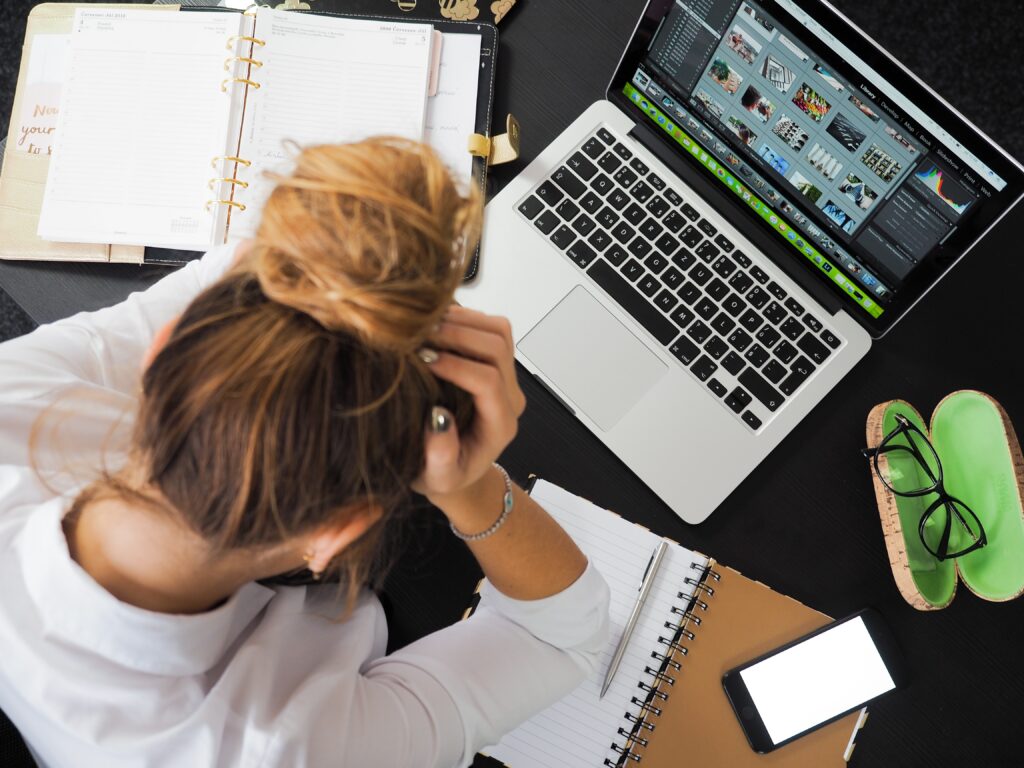 woman with bun looking stressed over a laptop with her head in her hands demonstrating how she is lacking time management strategies for working moms 