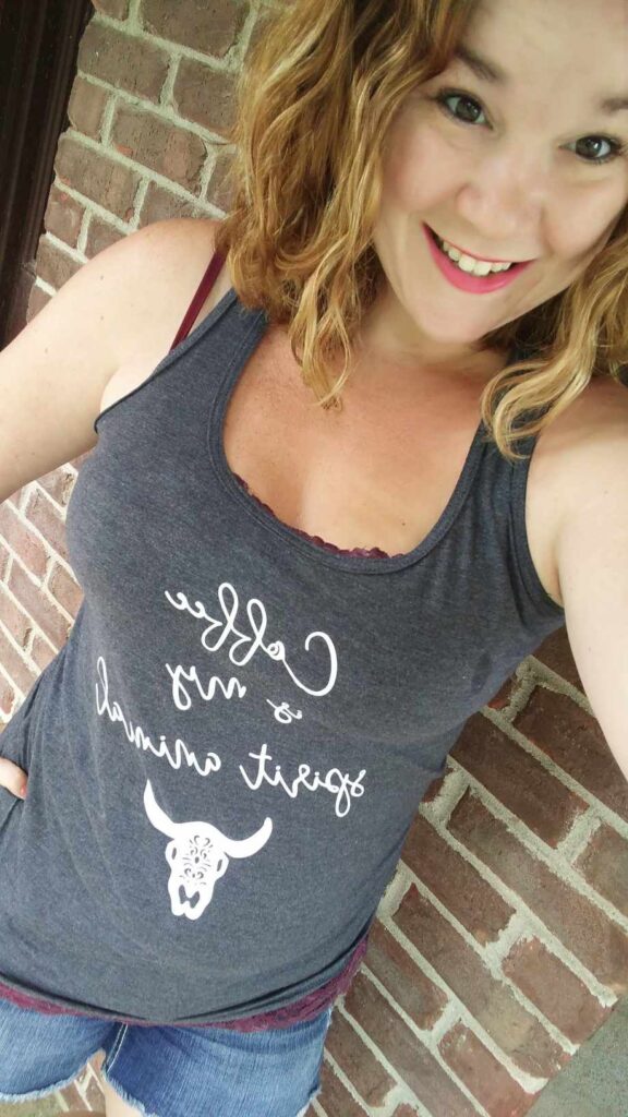 Woman with bright lipstick, a grew tank that says "Coffee is my spirit animal", chin length highlighted hair and a smile embrace your true self and embrace being too much