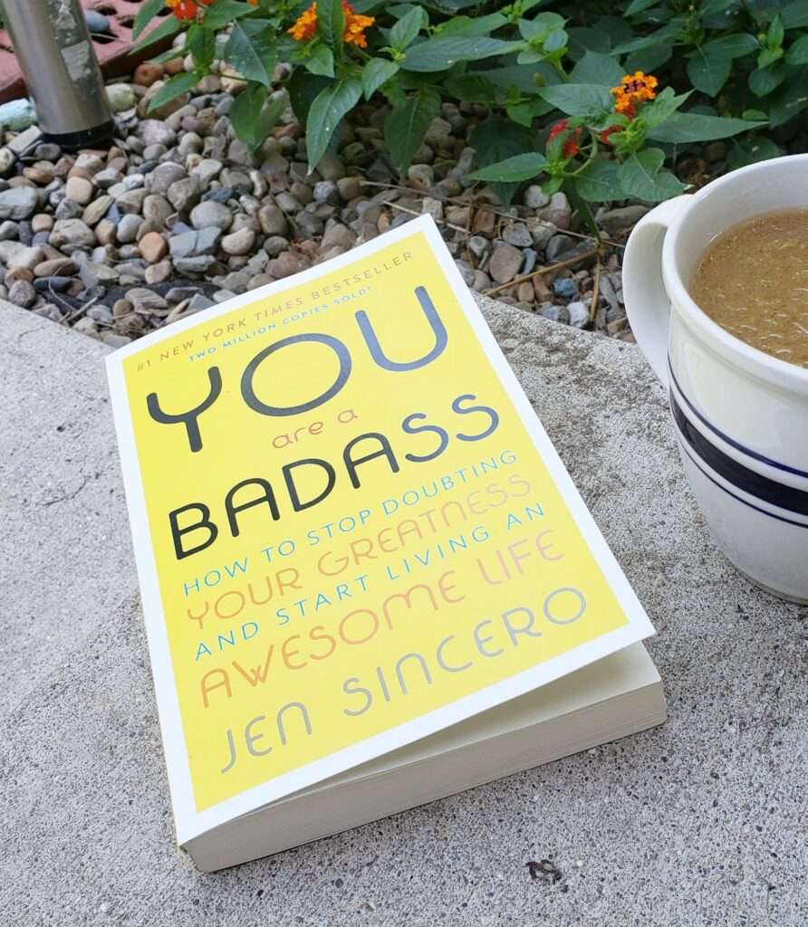 You Are a Badass Book sitting on a concrete step next to a cup of coffee for empowerment books for working moms