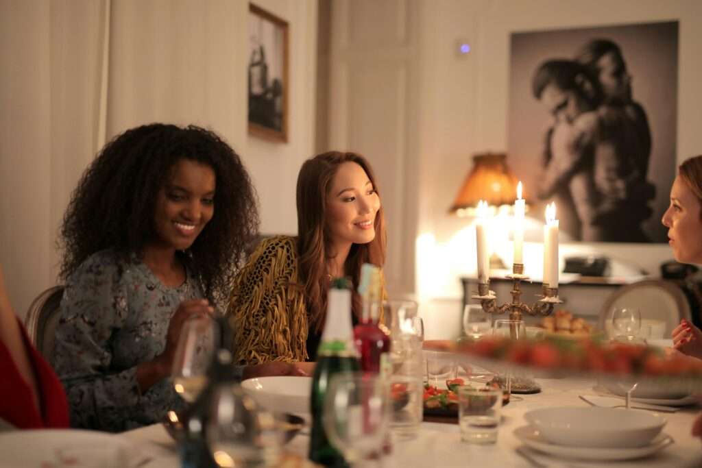 Group of women sitting around a table eating dinner, drinking wine and discussing self-improvement for moms.