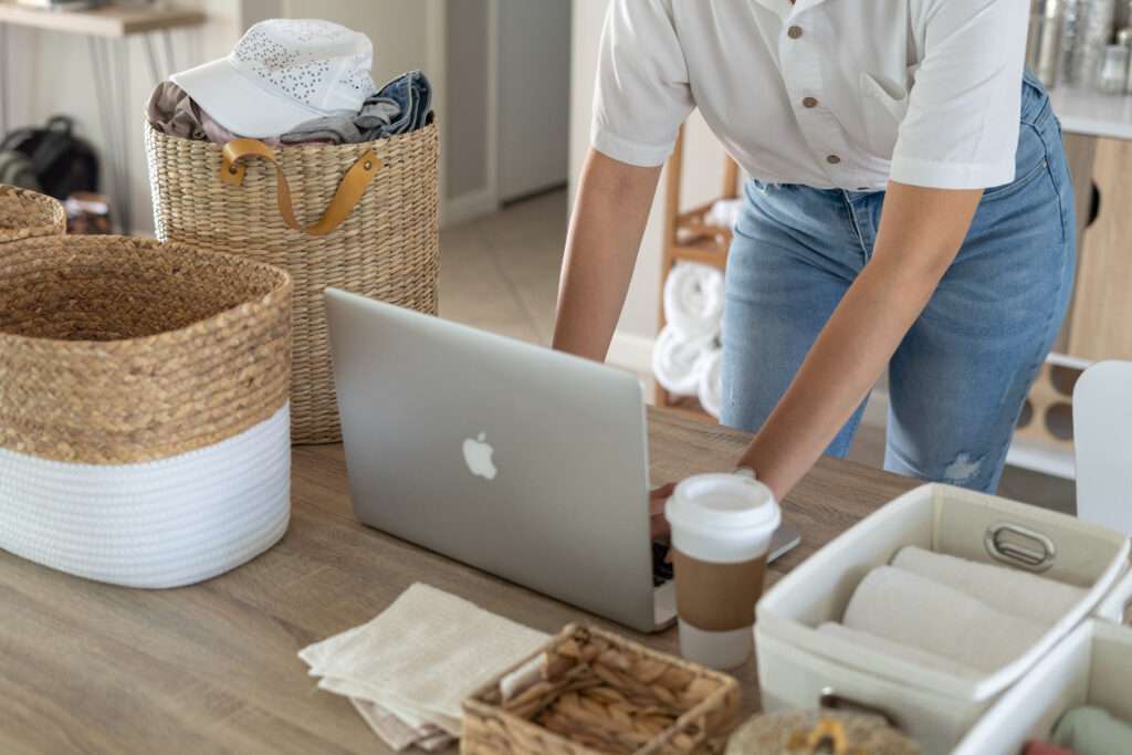 Woman wearing white shirt and jeans in front of laptop computer with laundry and diapers around her. 