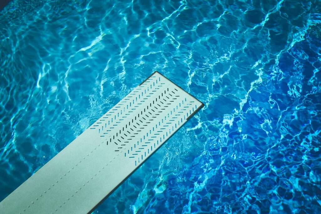 Diving board with little patterns cut out over a pool of clear blue water that someone embracing fear will dive off of. 