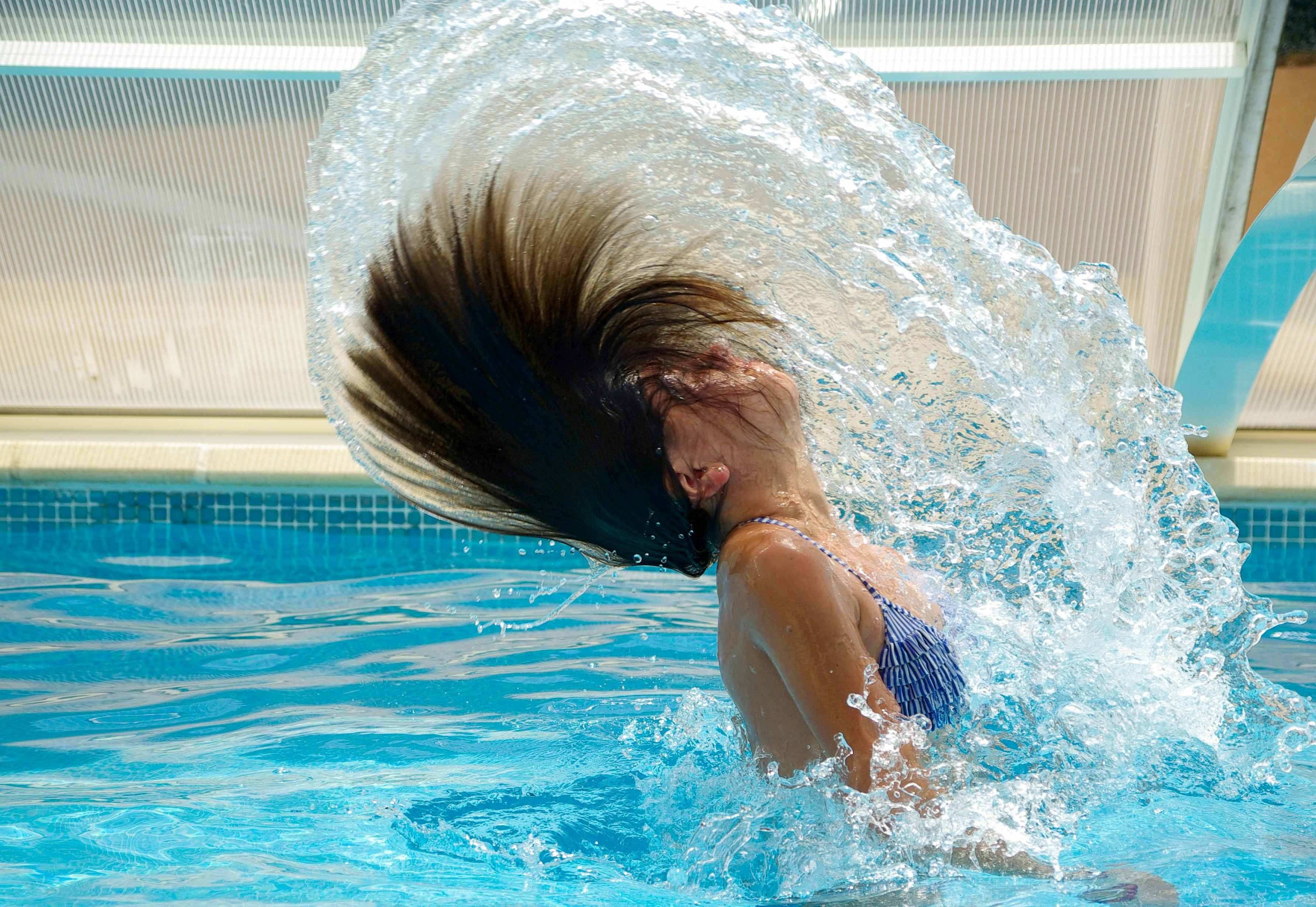 Woman in blue striped bikini top emerging from the water and flipping her hair back in a way that causes an arc of water after she was embracing fear and making the dive