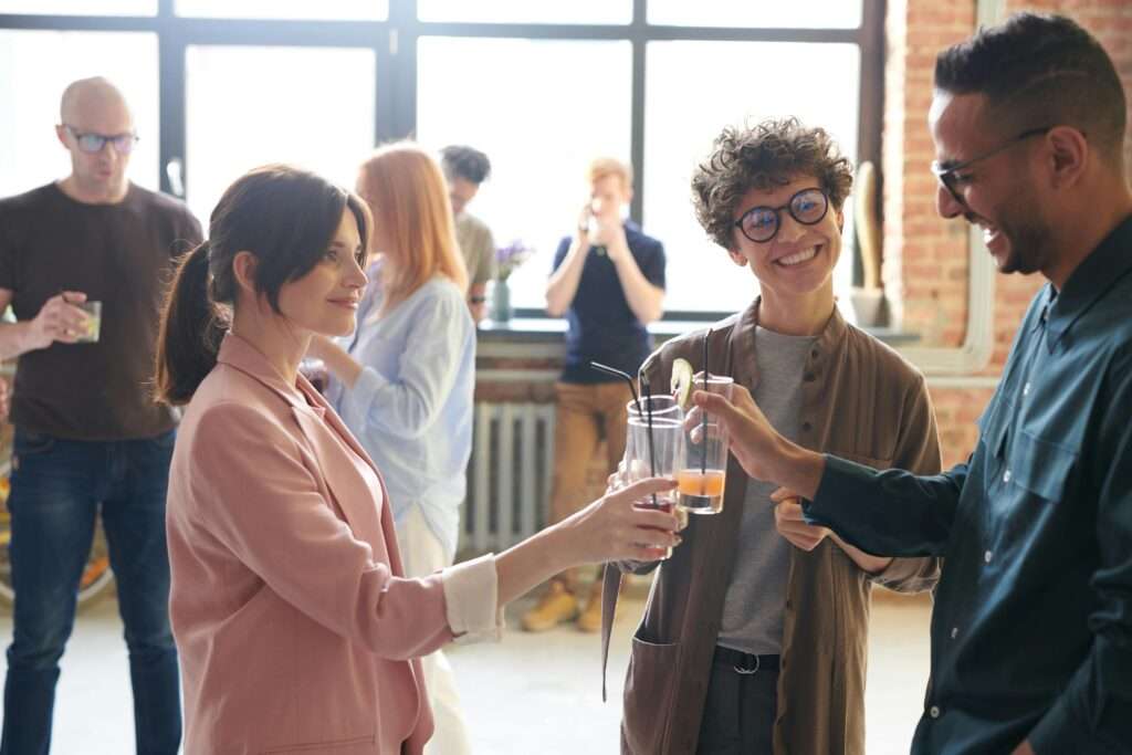 A few different groups of people standing around an open coworking like space with drinks talking, laughing and networking demonstrating the power of positive influence. 