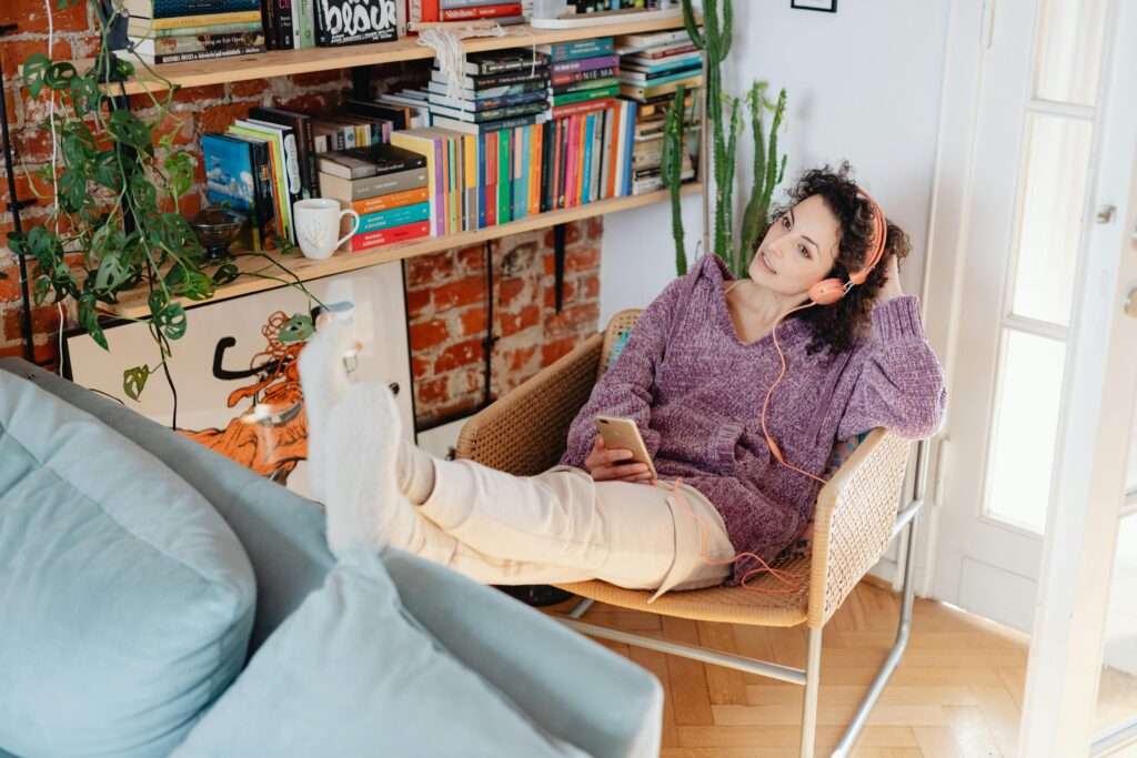 Woman with her feet up lounged back in a chair with headphones on listening to something on her phone practicing the power of positive influence. 